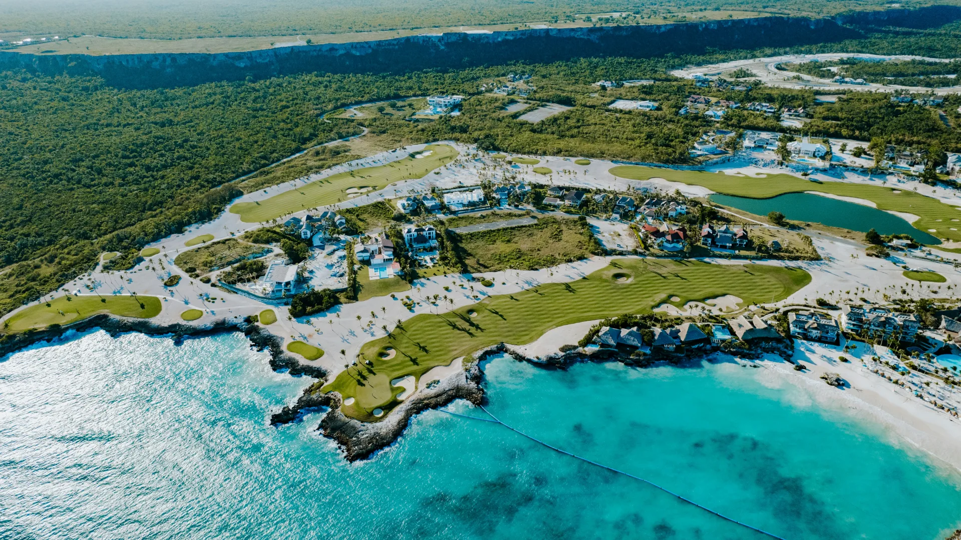 Aerial view of a coastal golf resort with villas above turquoise water