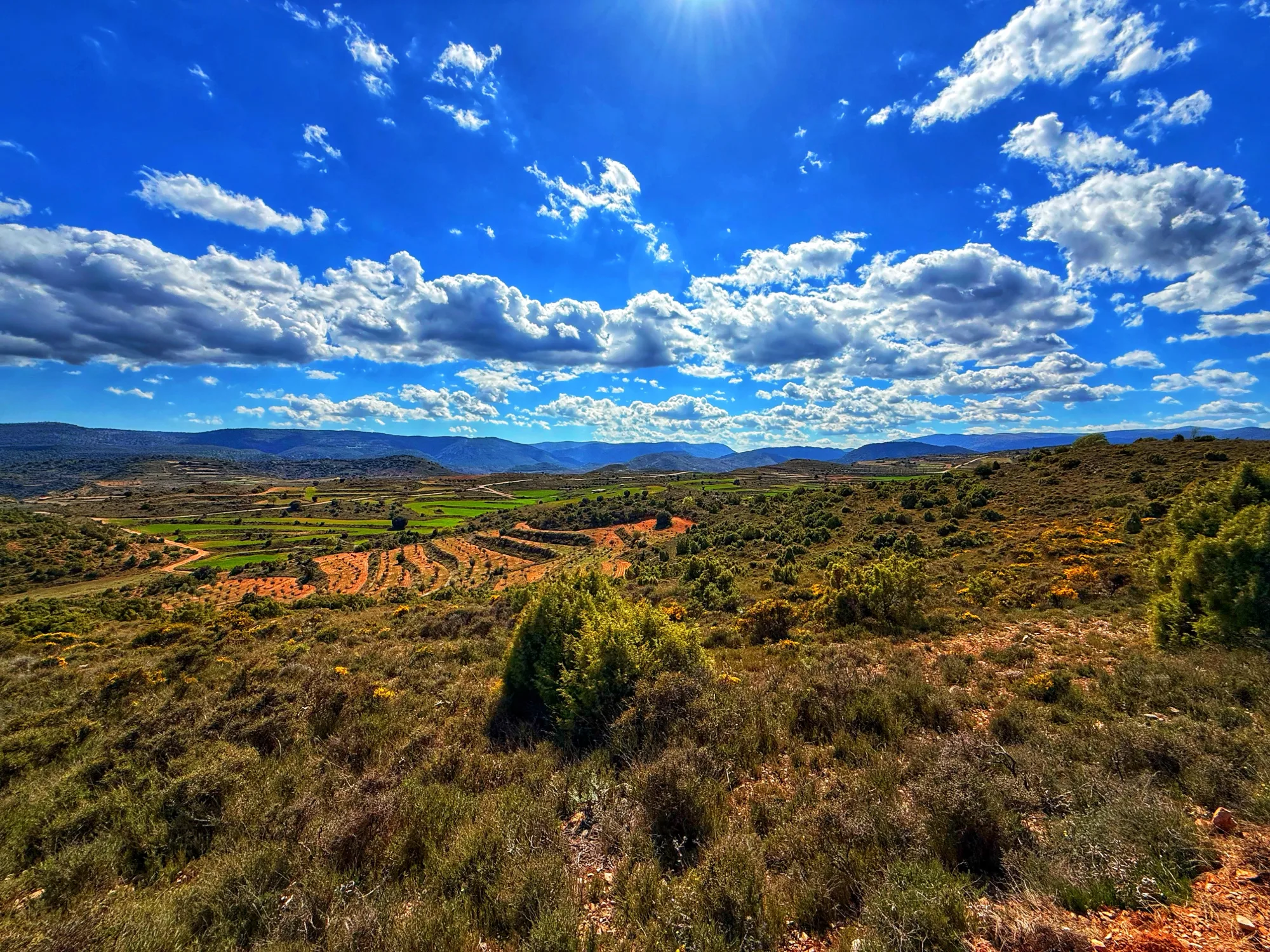 Terraced farmland and scrub beneath mountain ranges